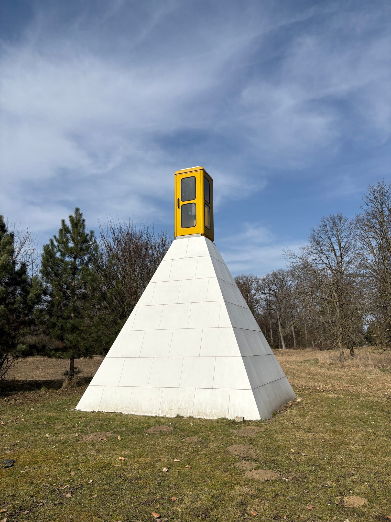 Eine weiße Kunststoffpyramide mitten im Schlosspark Grafenegg. Auf deren Spitze befindet sich eine gelbe Telefonzelle.